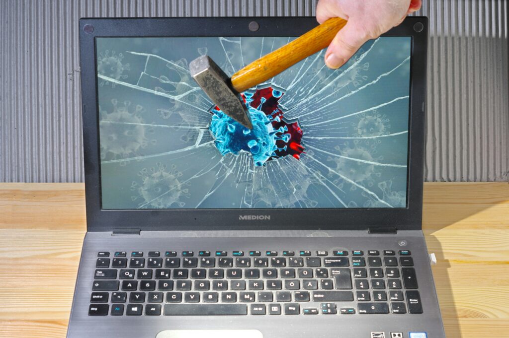 A hammer striking a laptop screen with a virus graphic, symbolizing cyber threats and IT risk.