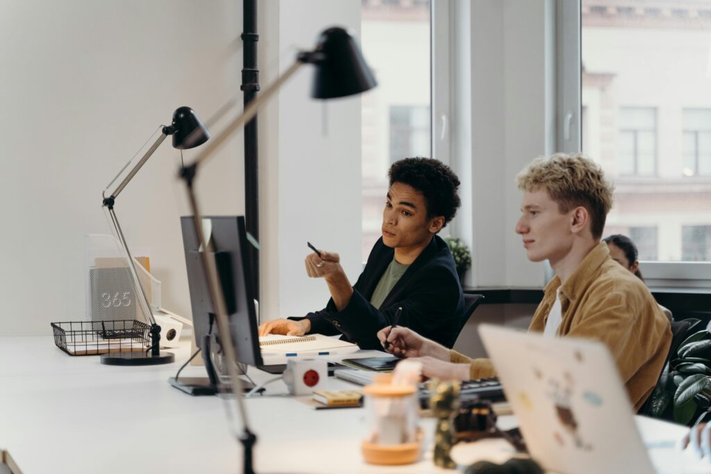 Two coworkers in a modern office discussing endpoint security solutions at a desktop computer while laptops sit on the desk.