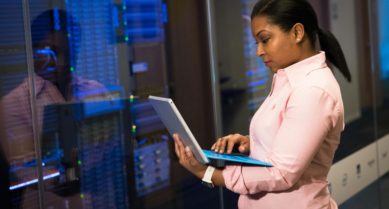 IT professional using a laptop in a server room while monitoring systems for patch management.