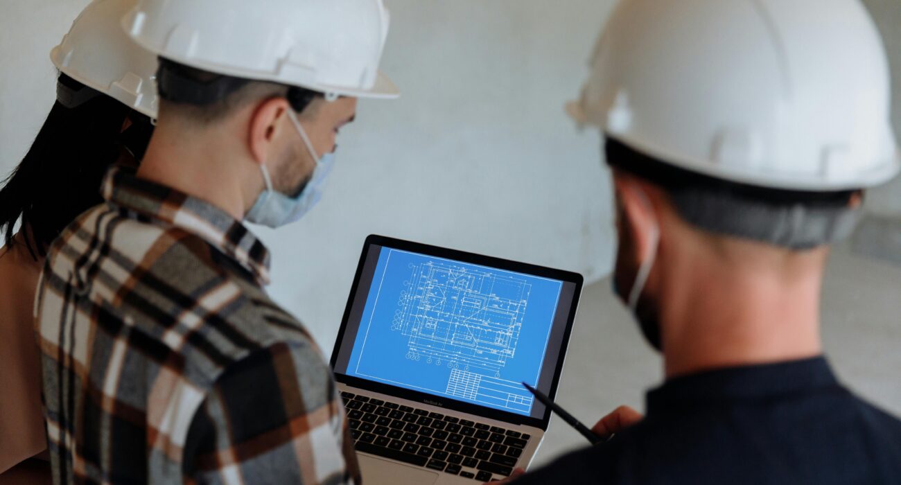 Construction team in hard hats reviewing digital building plans on a laptop during a site discussion