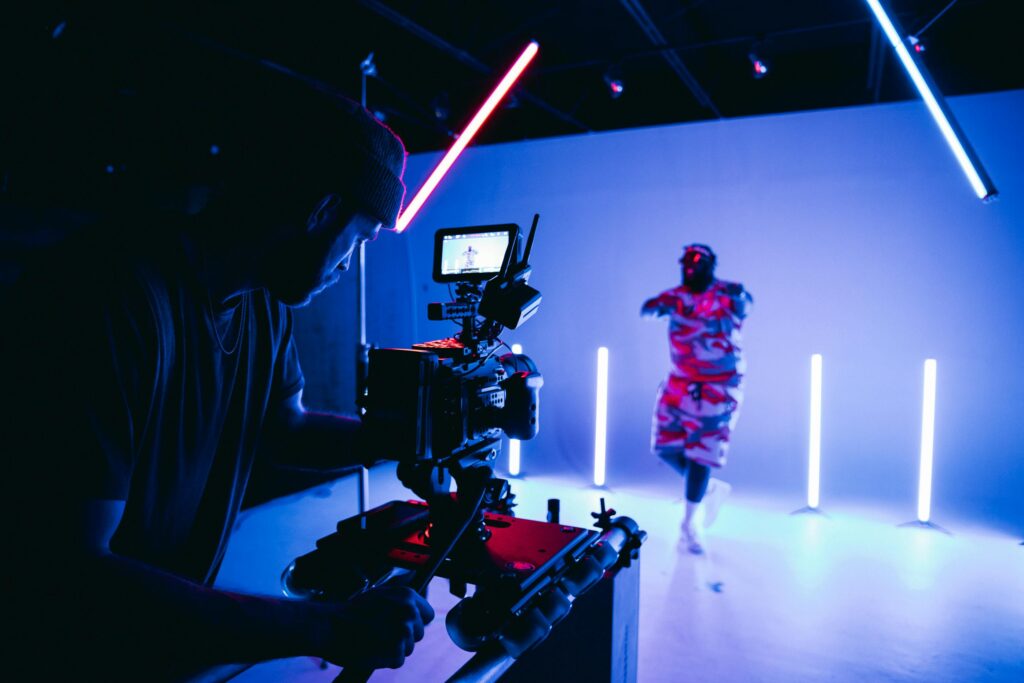 Camera operator filming a performer in a neon-lit studio during a video production session