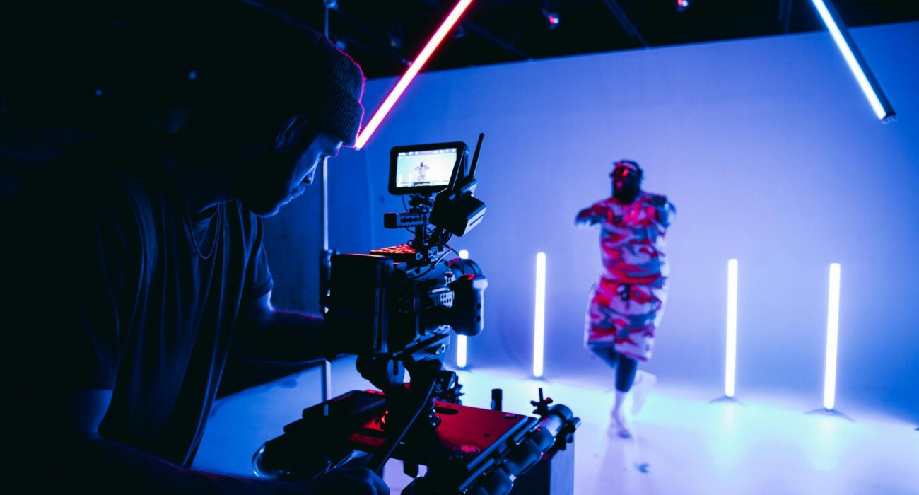 Camera operator filming a performer in a neon-lit studio during a video production session