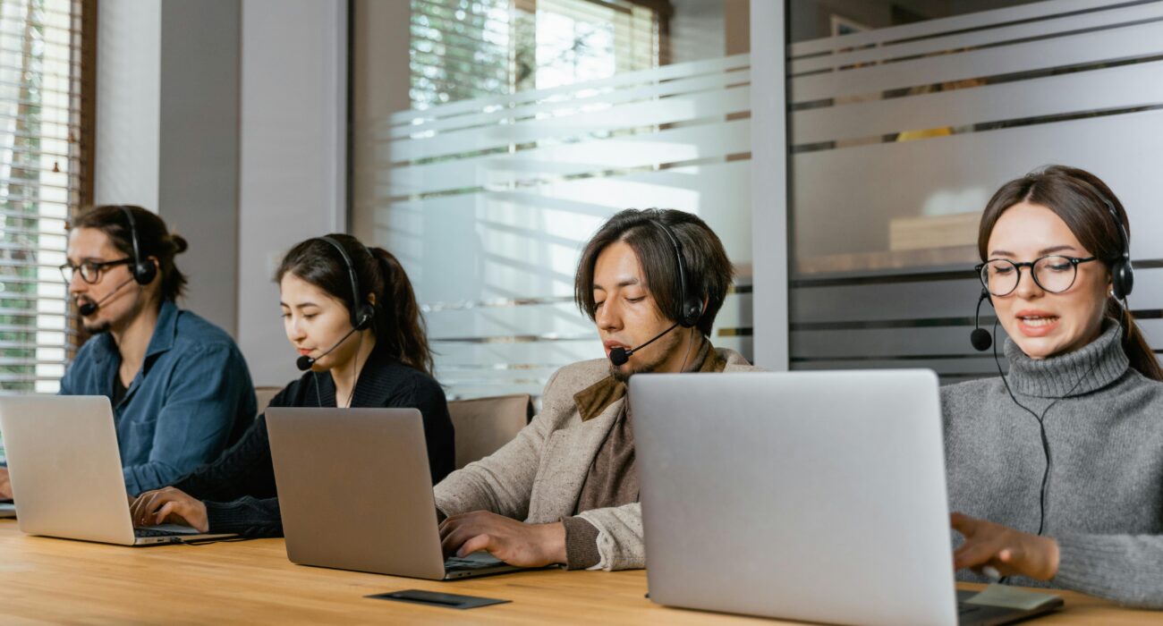 Professional IT support team wearing headsets and working on laptops in a modern office setting